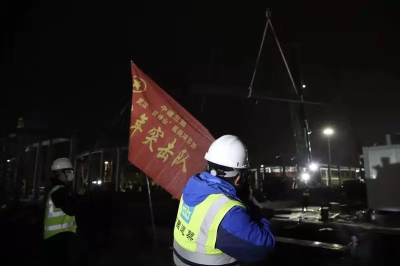 2月1日21時，火神山醫院施工現場仍是一派熱火朝天，中建三局施工人員正在挑燈夜戰，工地上施工人員24小時不眠不休，為了在2月3日交付使用全力沖刺。圖為青年突擊隊旗幟在火神山飄揚。