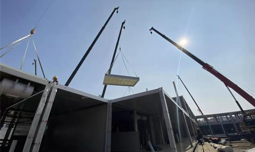 截至1月30日中午12時，武漢火神山醫院項目場地平整、砂石回填、HDPE膜鋪設全部完成，基礎混凝土澆筑完成95％；集裝箱板房進場、改裝、吊裝正快速推進。管線溝槽開挖、埋設級回填完成50％；污水處理間設備吊裝完成，管道安裝完成60％；調蓄水池HDPE膜開始鋪設。圖為住院樓板房吊裝現場。