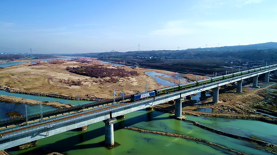在隧道施工中，中鐵十四局建設者采用超前水平鉆排水和水壓爆破法施工，提高了單循環爆破進尺，確保了施工進度。在全線唯一一座轉體橋洋縣漢江特大橋跨京昆高速轉體橋施工中，他們采用活性粉末混凝土球鉸等先進設備，提升了施工效率。圖為列車駛過中鐵十四局承建的洋縣漢江特大橋。（肖永順 攝）