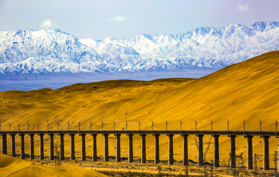 自2012年底敦格鐵路開工建設以來，中國鐵建科學組織、優化施工方案、合理安排作業時間，先后順利完成了全線多個重點控制性工程施工。在當金山隧道施工中，建設者大力進行科技創新，攻克高寒缺氧等難題，創造了我國隧道獨頭掘進最長、高原隧道施工通風距離最長的紀錄。圖為沙山溝特大橋與沙山、雪山融為一體，美輪美奐。（金偉 攝）