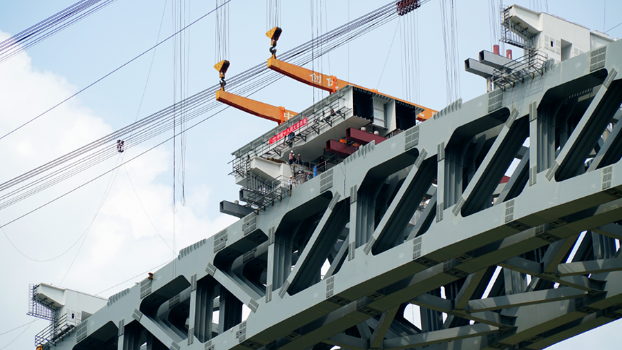 兩側引橋鋼混結合梁采用“步履式頂推”新工藝，均由大橋兩端向跨中方向頂推，在兩側分別搭設鋼混結合梁頂推平臺，并完成鋼混結合梁的拼裝、焊接、高強螺栓施擰及補涂裝等施工任務。圖為鋼箱梁節段落梁。