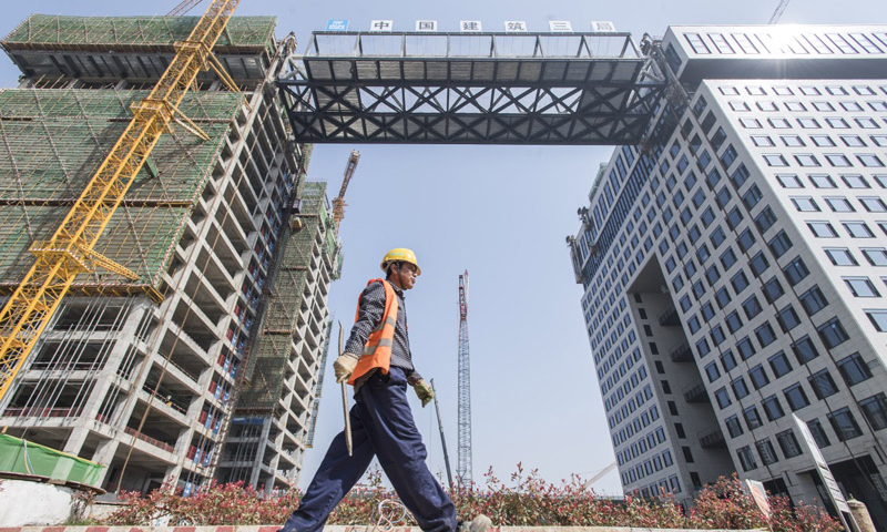 3月28日，經過48小時的走走停停，總重1500噸、高9.9米、寬18米、跨度76.5米的鋼結構連廊整體提升至離地73.6米的高空，橫亙于武漢光谷新城核心區域“中建·光谷之星”項目兩棟塔樓之間。圖為中建三局的建設者從提升完成的“空中生態綠廊”周邊走過。（新華社記者 肖藝九 攝）