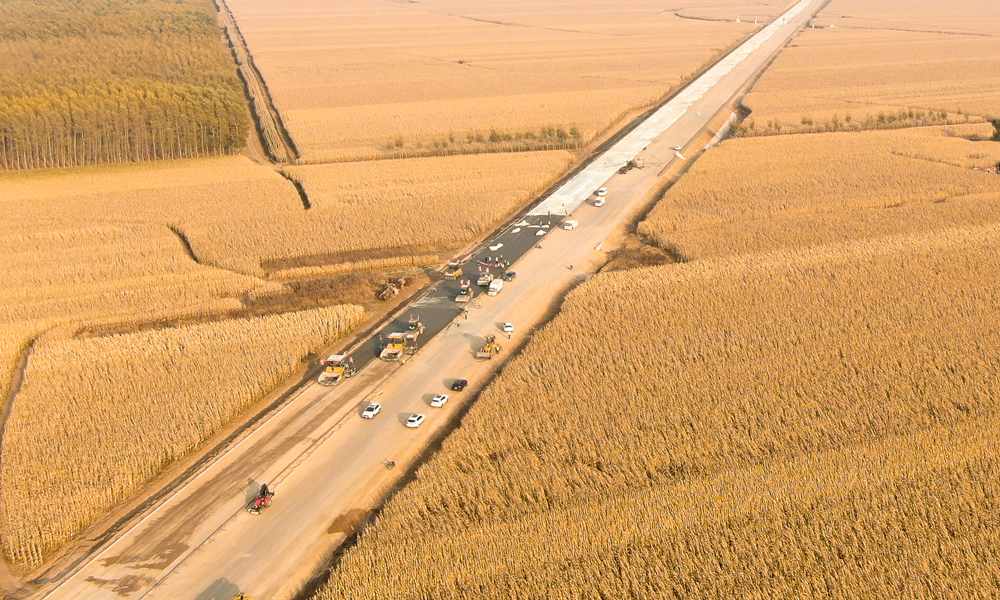 在田間地頭，農民們忙著收玉米，將一年的勞動成果打包帶回家；在施工現場，建設者們揮汗如雨，全面加快路面施工。長太高速公路是吉林省中西部地區的一條重要干線通道，整條線路穿過著名的“黃金玉米帶”、我國大型商品糧和油料基地，并輻射內蒙古東部通遼市、興安盟等多個旗縣。圖為長太高速沿路布滿玉米田。