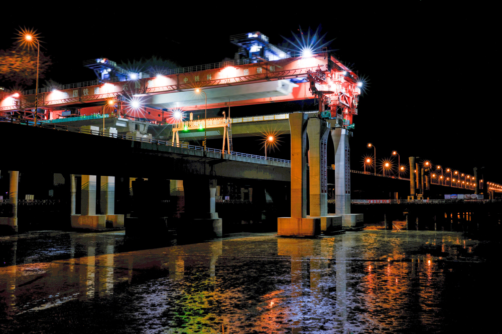 項目團隊圍繞海上50米大跨徑、1800噸超大噸位整孔預制箱梁運輸兩個方面開展科研攻關，研制了我國自主研發、目前世界上最大的公路架橋機“越海號”開展“梁上運架”施工，成功攻克箱梁單體重量大、超高橋面漸變橫坡、高低墩及1800米超小曲線半徑等技術難題，確保了箱梁架設和金塘大橋運營安全，創下了國內采用“梁上運架”技術單體最重的整孔預制箱梁施工紀錄。圖為跨金塘大橋架梁施工現場。