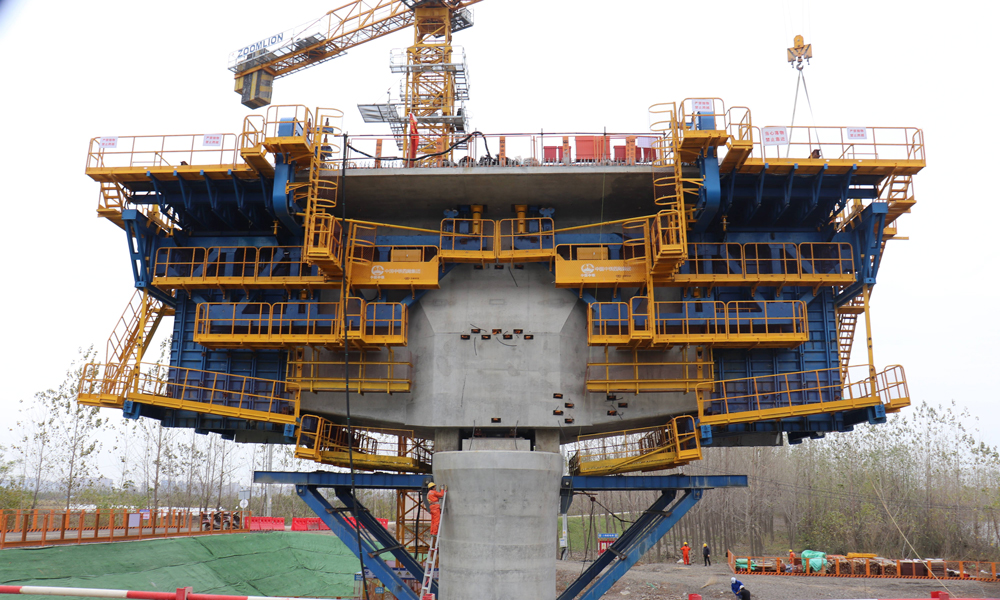 智慧造橋機由承重桿件、液壓整體模板、液壓調節、自動走行、信息化監控、鋼筋骨架整體吊裝、平臺防護等系統組成，并預留了智能蒸汽養護、自動噴淋等多功能系統安裝接口，集液壓傳動、智能操控、信息化監測技術于一體，極大解決了傳統掛籃在懸臂現澆連續梁施工中結構復雜、裝拆繁瑣等問題，大幅提高了懸臂現澆梁自動化、信息化和智能化建造水平，推廣前景廣闊。