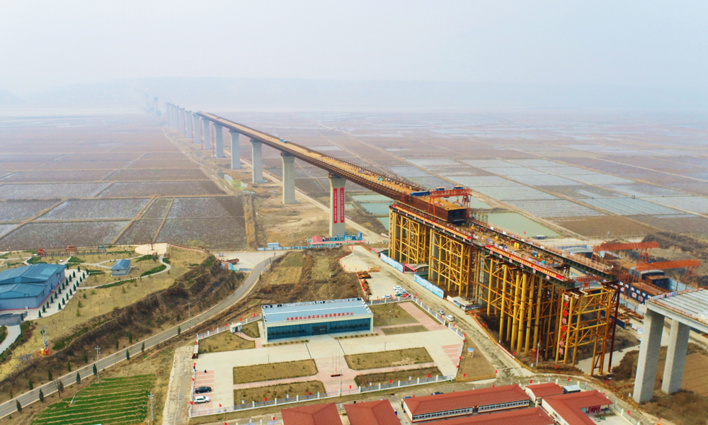 臨猗黃河大橋位于山西省運城市臨猗縣內，橫跨山西陜西兩省，是國家高速公路菏寶線G3511的控制性節點工程，大橋全長5427米。采用大跨度整幅橋核心箱組合梁步履式頂推工藝施工，基本跨徑為128米，鋼梁總重5.7萬噸，連續頂推重量2.9萬噸，頂推精度要求高、施工難度大。圖為大橋山西側施工作業現場。