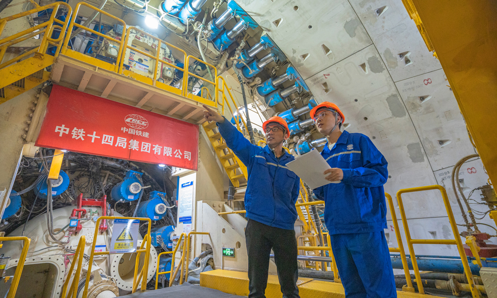 針對工程特點和項目需求，中鐵十四局對盾構機進行了針對性設計優化，聯合研發了具有自主知識產權的“新穿越號”盾構機，配置高承壓主驅動密封、大流量泥水沖刷環流系統、高效物料運輸及智能化預制構件同步拼裝技術、壁后同步注漿密實度檢測系統等多項關鍵技術，大幅度提高盾構機的適應性和可靠性，為工程順利實施保駕護航。圖為技術人員正在檢查“新穿越號”盾構機的掘進狀態。