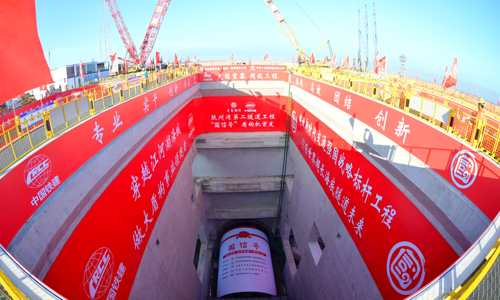 6月30日，膠州灣第二隧道“國信號”盾構機在青島港8號碼頭順利首發，標志著由青島國信集團投資建設，中國鐵建所屬鐵四院設計、中鐵十四局施工的世界最長海底道路隧道——膠州灣第二隧道工程盾構段正式掘進施工，開啟了膠州灣東西兩岸“對向掘進”的跨海征途。圖為膠州灣第二隧道“國信號”盾構機始發現場。