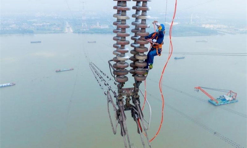 國家電網江蘇南京供電公司工作人員在500千伏汊龍汊王線跨江高塔上使用高壓泵給絕緣子噴涂防污閃涂料，提高其絕緣性能。
