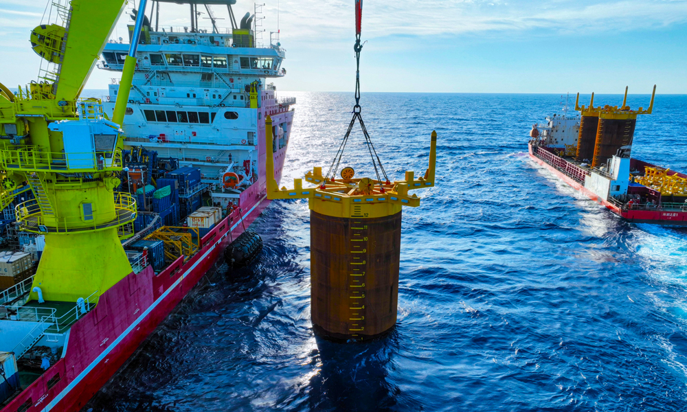 項目部根據吸力樁重心位置量身定制3套吊裝索具，確保起吊時樁體垂直于海平面。現場強化定位精度控制，布控6個定位信標，形成“六邊形”定位陣校準方陣。投入兩臺ROV（水下機器人），采用“阻尼艏向調整法”進行艏向細微調整，保證艏向精度。貫入作業中，船舶吊機和ROV協同作業，精準控制鉤頭載荷和貫入壓力，確保吸力樁緩慢平穩沉降。最終實現了3套吸力樁一次性高精度貫入成功。圖為吸力樁安裝作業現場。