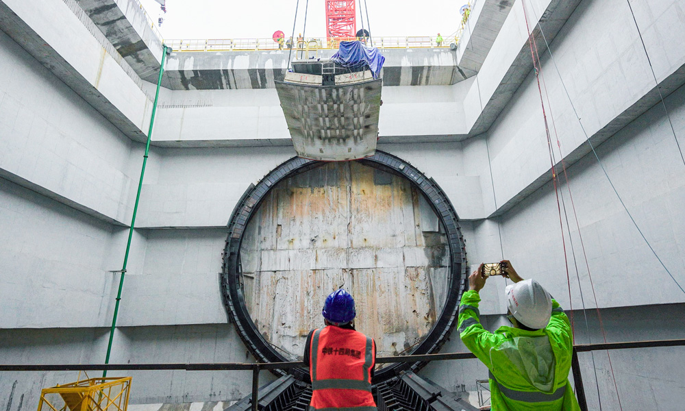 為隧道建設量身定制的盾構機“英雄號”全長134米，開挖直徑14.8米。連日來，盾構機主驅動、刀盤、拼裝機等已運輸下井、完成組裝，后期將進行盾構機管線連接和整機調試工作，即將開始盾構隧道掘進。圖為施工人員在現場緊盯盾體下井定位組裝。