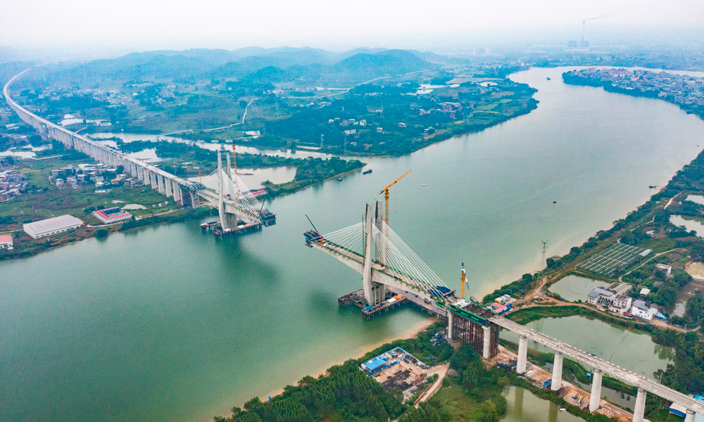 該特大橋鋼混結合段單側懸臂施工長15米，由2.7米長混凝土梁和12.3米鋼梁組成，懸灌重量為1800噸，由于鋼混段施工位于航道中間，需要采用懸吊施工工藝。建設團隊創新思路方法，將鋼梁分為4.65米和7.65米兩次吊裝，再進行混凝土分段澆筑的施工工藝，解決超長、超重鋼混段懸灌施工難題。圖為施工現場航拍中景。