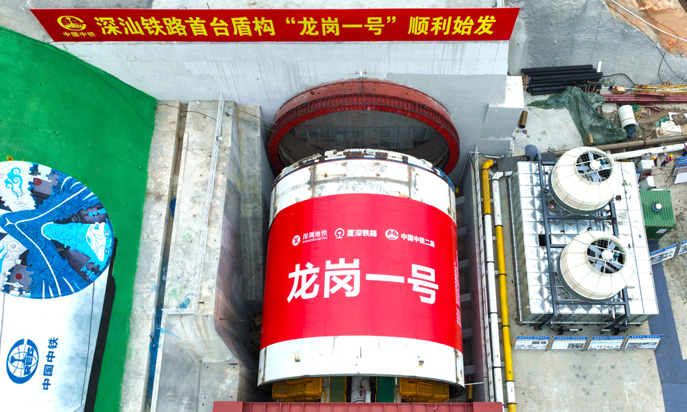 深汕鐵路是“八縱八橫”高鐵主通道中沿海高速通道的重要組成部分，起于深圳樞紐西麗站，終至深汕合作區并引入廣汕鐵路深汕站，正線全長125.52公里。由中鐵二局組織施工的深汕鐵路龍崗隧道盾構掘進全段并行廈深高鐵，先后穿越21處重要建構筑物，長距離穿越巖溶及軟硬不均與軟硬交互不良地質，是深汕鐵路重點控制性工程之一。龍崗隧道進口段分為南約和寶荷隧道兩個區間，“龍崗一號”盾構機負責南約盾構區間的掘進任務。圖為“龍崗一號”盾構機始發現場。