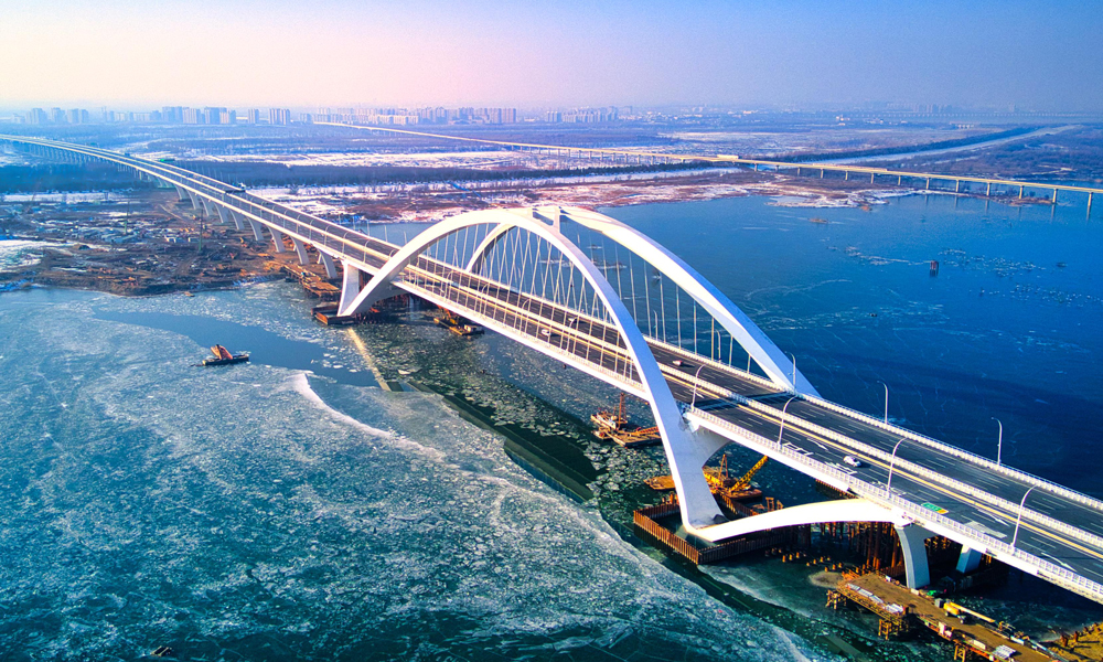 京雄高速公路（北京段）自2020年12月開工建設以來，中國中鐵建設者綜合利用30余項專利技術優勢，先后攻克“筑造精品工程、建設周期保障、危大工程管控、征拆難點破解、關鍵技術攻堅”五大重難點。全長1.62公里的京雄大橋是國內首座空間異形拱肋飛燕提籃式鋼箱拱橋，是北京地區單跨跨度最大橋梁，通過運用數字化孿生技術，采用異形曲面拱肋數字化加工制造、拱肋吊裝支架監測等新技術，極大提升了工程建造品質。房山北站是北京市首座陸地高架橋主線收費站，創新性采用橋梁分幅設計，將快慢車、客貨車進行分離式指引通行，將大幅提升通行效率。圖為京雄高速公路京雄大橋。