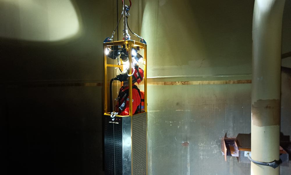 為了確保平臺凝析油艙處于良好運行狀態，掌握艙內設備運轉情況，平臺工作人員會定期開展清艙檢測作業。圖為“深海一號”現場作業人員搭乘空間極其狹小的特制工作吊籃進入凝析油艙內部進行檢查。周宇 攝