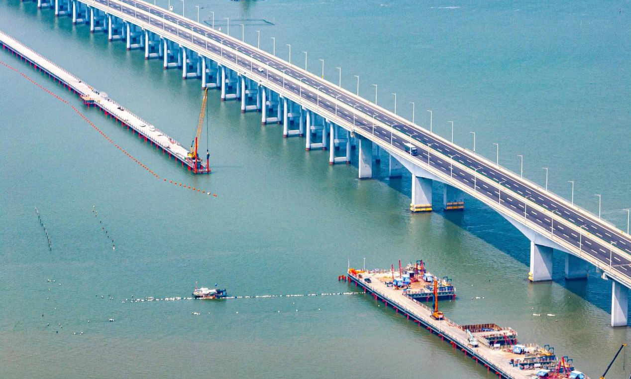 近日，中鐵四局新建漳汕高鐵漳江灣跨海特大橋主棧橋施工現場機械林立，近百名施工人員全力沖刺棧橋合龍節點目標。漳汕高鐵線路全長約175公里，全線涉及3座跨海大橋，其中漳江灣跨海特大橋為全線控制性工程，橋梁全長5.8公里，海域部分橋梁長5公里。為解決海上材料、設備運輸和人員通行和主體工程作業要求，四局建設者在漳江灣海域搭設長4.7公里、寬8米的主棧橋。目前，大橋樁基、承臺、墩身施工正在有序推進建設。