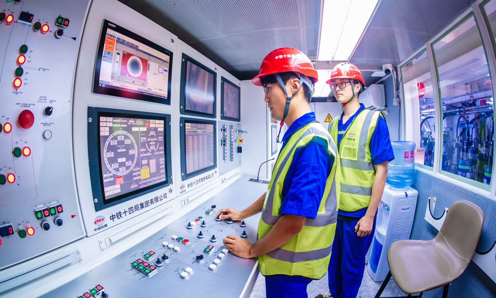 針對(duì)施工重難點(diǎn)，中鐵十四局結(jié)合深耕黃河流域盾構(gòu)施工經(jīng)驗(yàn)，量身打造“山河號(hào)”盾構(gòu)機(jī)，配備了配備帶壓復(fù)合型刀盤(pán)、伸縮式主驅(qū)動(dòng)等先進(jìn)技術(shù)，并搭載了超前地質(zhì)預(yù)報(bào)、地層界面識(shí)別等智能化裝備系統(tǒng)，盾構(gòu)機(jī)總裝達(dá)到世界先進(jìn)水平。圖為駕駛艙內(nèi)，技術(shù)人員操作盾構(gòu)機(jī)向前掘進(jìn)。