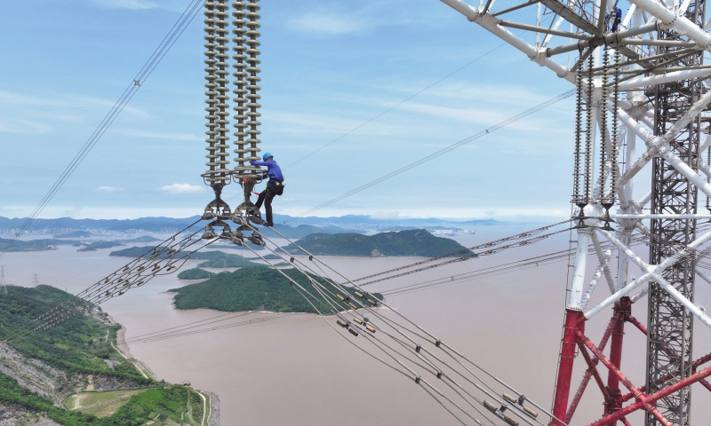 此次檢修規(guī)模大、技術(shù)難度高，洛春5495線、洛曉5496線為跨海輸電線路，連接兩條線路的兩座高370米的輸電鐵塔分別位于舟山大貓山和寧波涼帽山，兩座輸電鐵塔檔距達(dá)2756米。檢修人員登上位于大貓山的輸電鐵塔，在高低落差達(dá)280米、最低點距海面高度超84米的線路開展走線作業(yè)。圖為檢修人員通過絕緣子串下到跨海輸電導(dǎo)線上。
