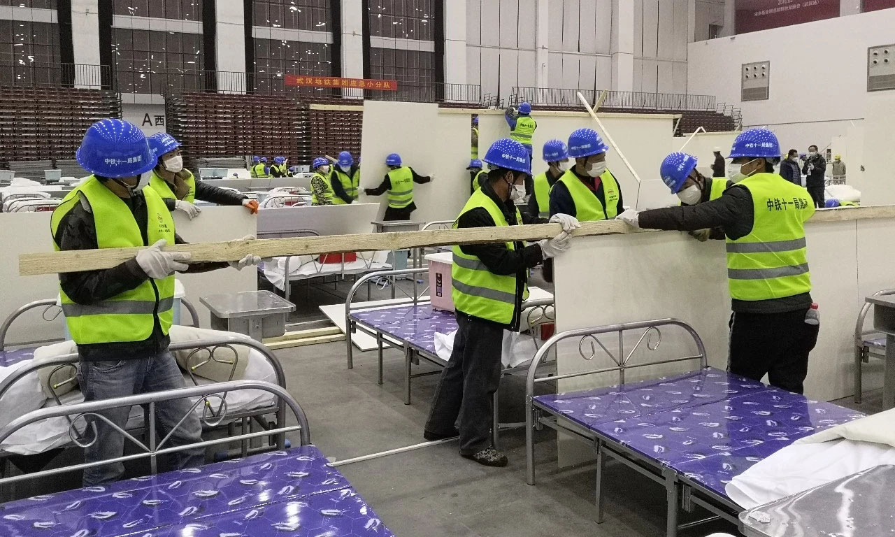 整個武漢客廳“方艙醫院”計劃在A、B、C三個廳布置2000個床位。此次增援主要負責武漢客廳“方艙醫院”A區12個倉位380多個病床隔板安裝、臨電安裝和門洞、吊頂、大門等施工任務。要求在最短時間內完成施工任務，為早日收治新冠肺炎病人贏得時間。圖為隔板安裝現場。