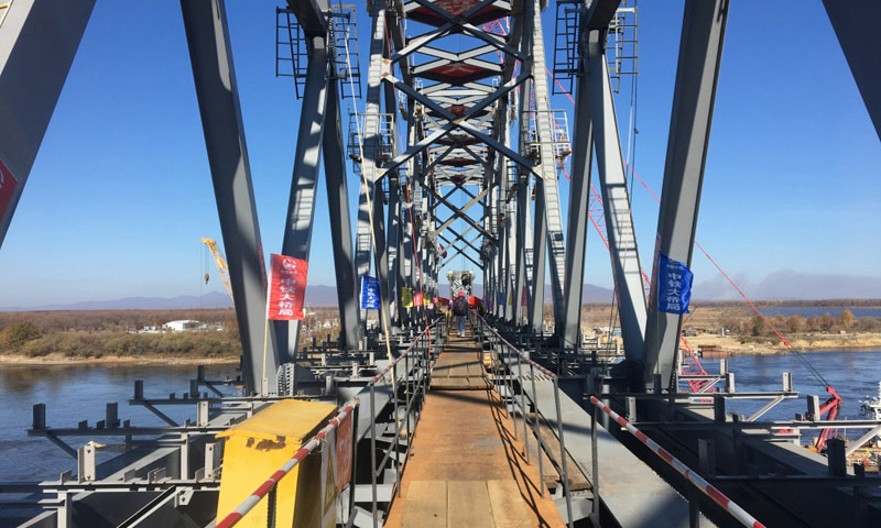 同江中俄鐵路大橋工程于2014年2月26日奠基，是中俄首座跨界河鐵路大橋，設計鐵路年過貨能力2100萬噸。大橋全長7193.71米，其中跨江大橋主橋全長2215.02米，中方境內1886.45米，俄方境內328.57米。圖為10月13日，同江中俄鐵路大橋中方最后一吊鋼梁安裝到位。（新華社記者 王君寶 攝）